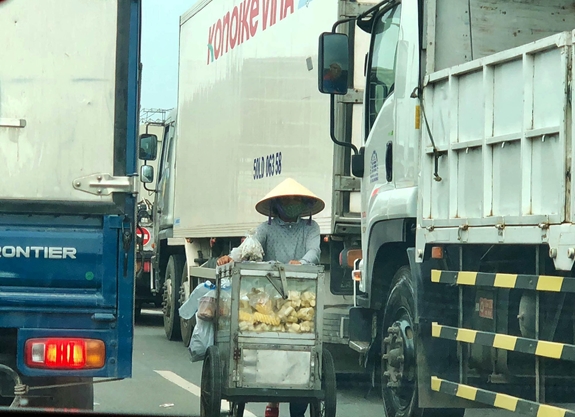 Người bán hàng rong ngang nhiên đẩy xe chở hàng đi giữa Quốc lộ 1A, ngược chiều với dòng ô tô lưu thông trên đường.